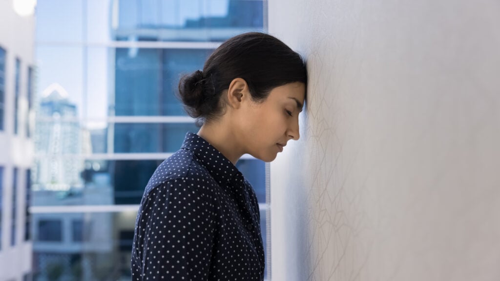Stressed executive woman leaning her forehead against office wall, symbolizing leadership burnout and need for executive burnout solutions through clarity.