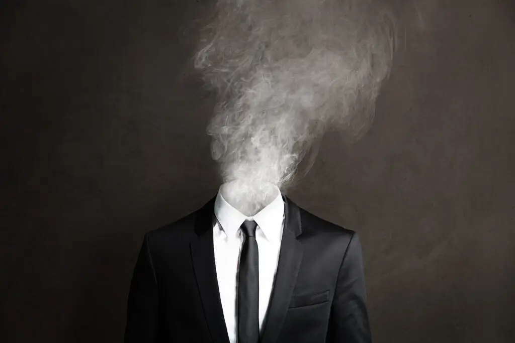 Concept image of executive burnout showing a businessperson in suit with head replaced by smoke, symbolizing stress, exhaustion, and lack of clarity.